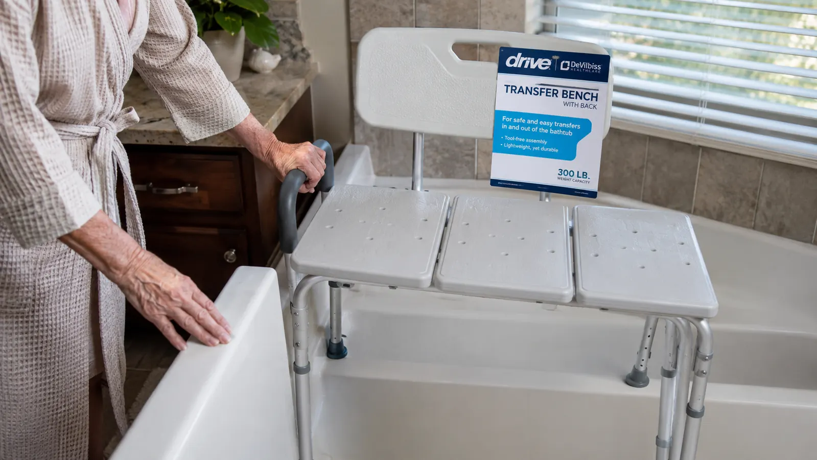 Drive Medical tub transfer bench being positioned over a bathtub edge with two legs inside the tub and two legs outside