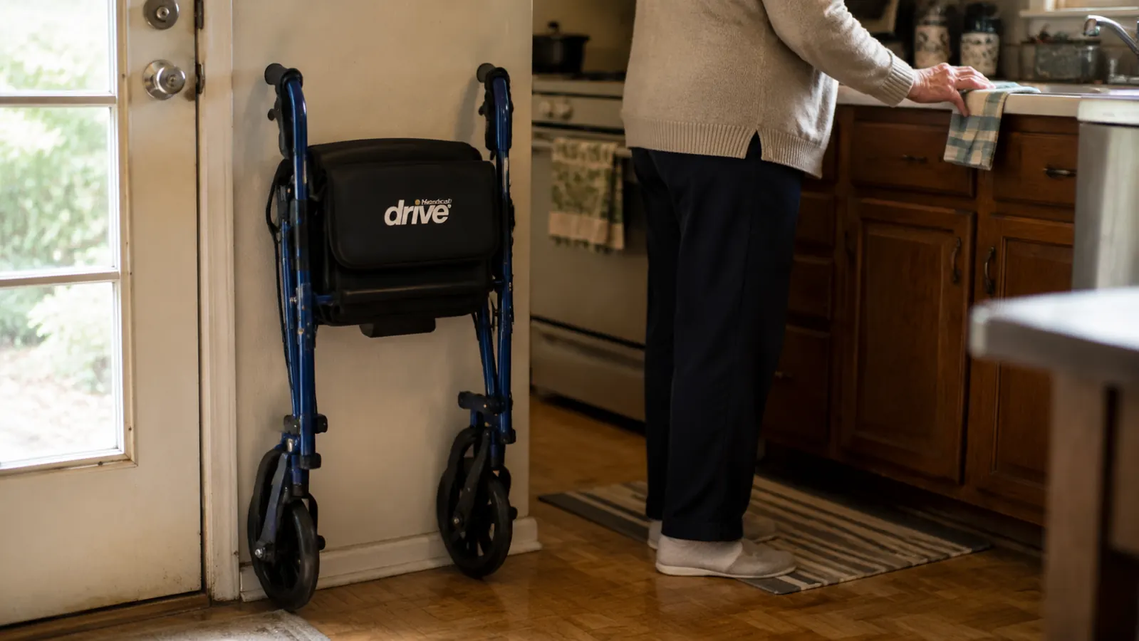 Blue Drive Medical rollator walker folded and leaning against a kitchen wall next to the back door